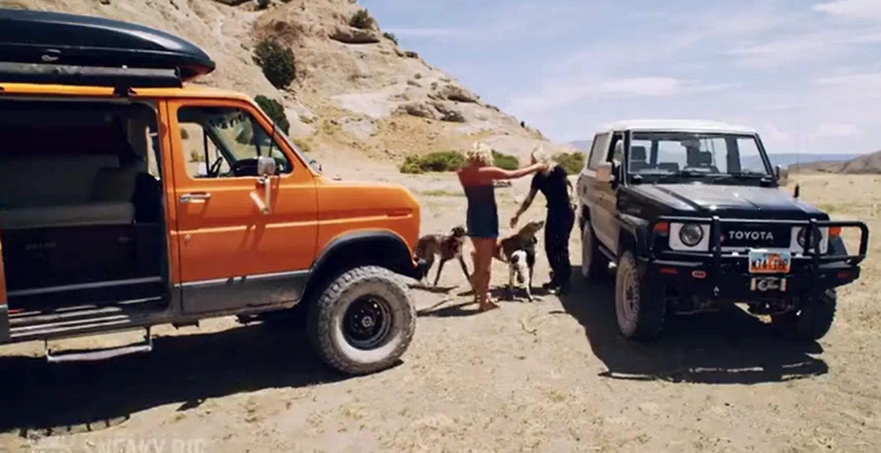 A couple of people and two dogs in front of an orange truck.