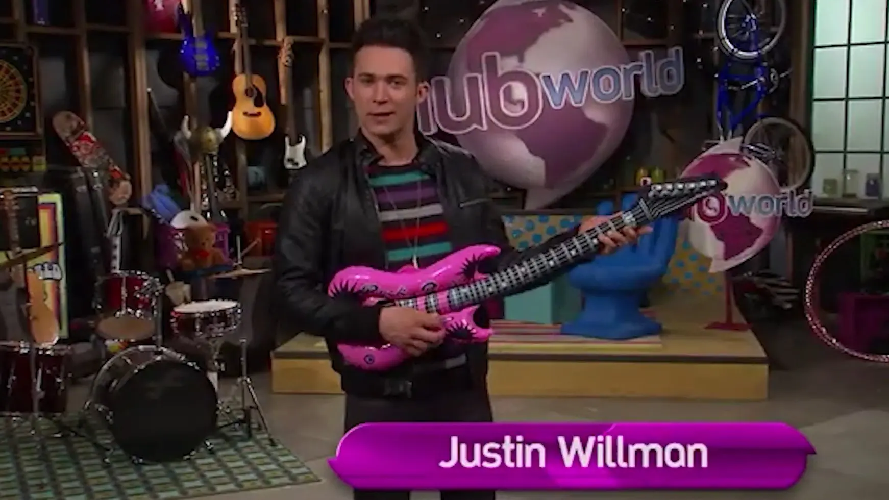 A man holding a pink guitar in front of a building.